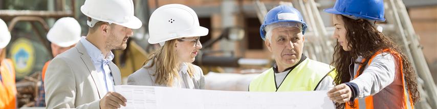 Several men and women in hard hats holding up building regulations outside, discussing plans moving forward. 2 people are business people and 2 are wearing high vis's and builders