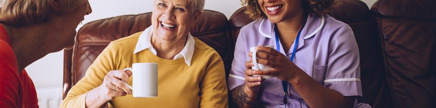 Serval women sat laughing with cake and tea each. Two women are living in the carehome while being looked after and visited by a careworker