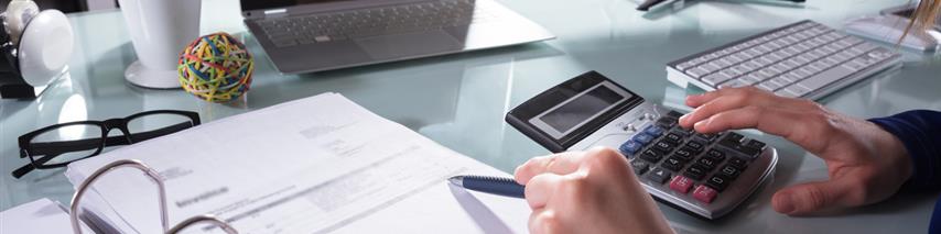 Person using calculator to figure out paper stats at desk surrounded by mutiple technology displays